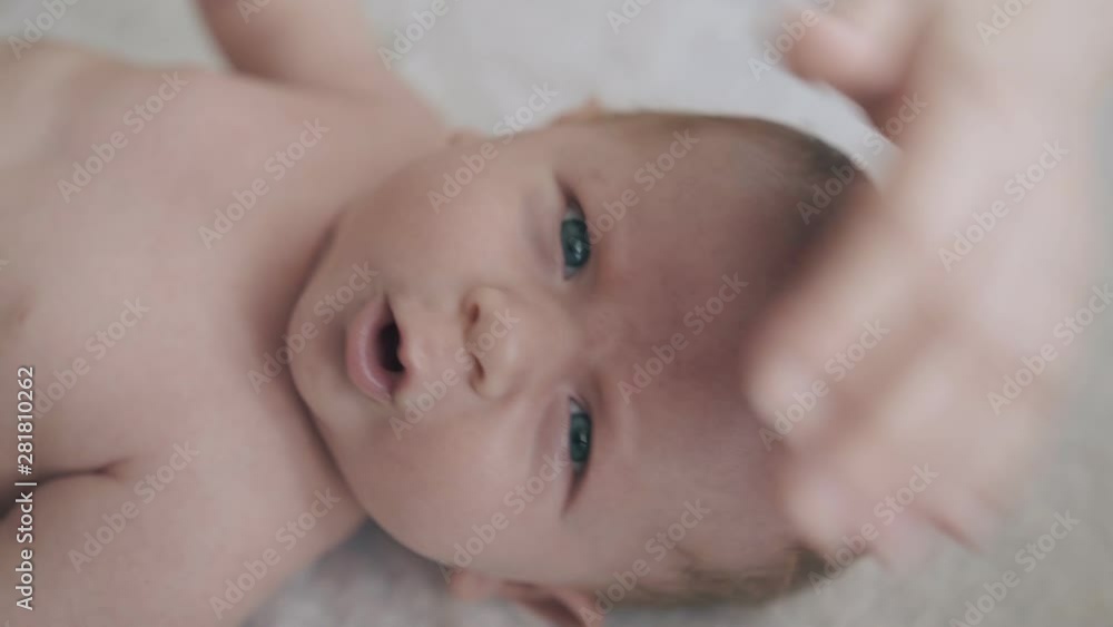 adorable infant boy with fair hair and large blue eyes lies on table and mother pets blond head extreme close view adorable infant boy with fair hair and large blue eyes lies on table and mother pets blond head extreme close view