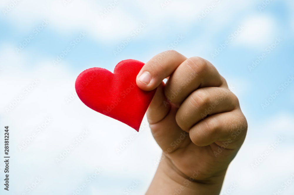 red heart in a child's hand against the sky
