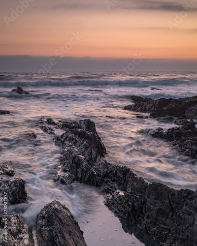 Waves crash over the rocks at Croyde Bay, North Devon in a seascape view at sunset with a nice golden sky