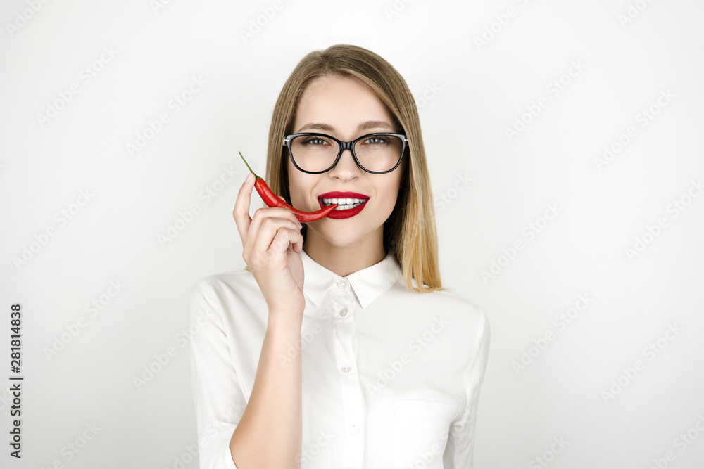 young beautiful blonde woman biting red chilly pepper isolated white background