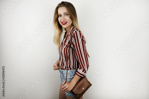 young beautiful blonde fit woman wearing trendy striped shirt denim shorts and leather mini bag isolated white background
