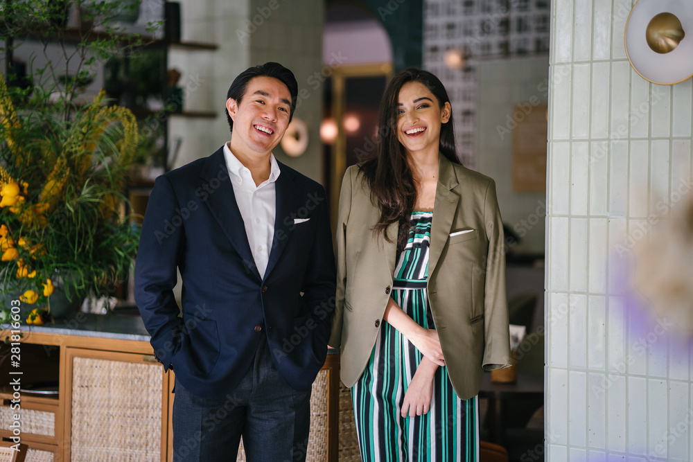 Φωτογραφία A young and handsome Chinese Asian man in a suit stands with a beautiful, elegant and attractive Indian woman in a classy outfit in a well-decorated interior during the day