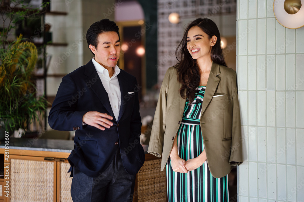 Φωτογραφία A young and handsome Chinese Asian man in a suit stands with a beautiful, elegant and attractive Indian woman in a classy outfit in a well-decorated interior