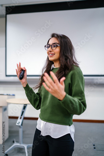 Portrait of a young, beautiful, attractive and intelligent-looking Indian Asian woman wearing spectacles in a sweater giving a business presentation to an audience.
