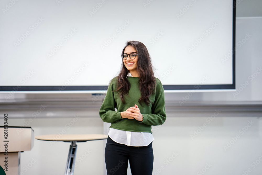 Wall Mural Portrait of a young, beautiful, attractive and intelligent-looking Indian Asian woman wearing spectacles in a sweater giving a business presentation to an audience