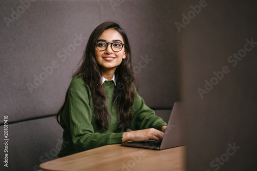 Portrait of a young, confident, intelligent-looking and attractive Indian Asian graduate student. She is smiling as she checks her smartphone. She is sitting in a study booth on her campus.