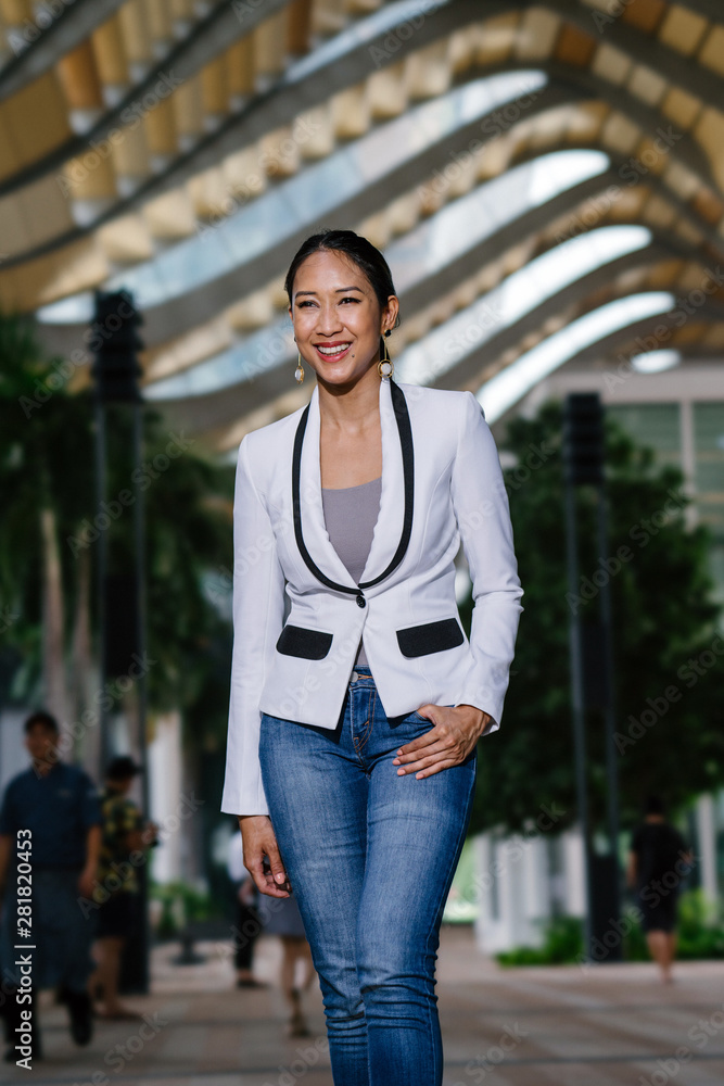 Fashion portrait of a beautiful, young, tall, elegant and sexy Chinese Asian woman in a white jacket over a casual outfit in the city against a modern, futuristic building.