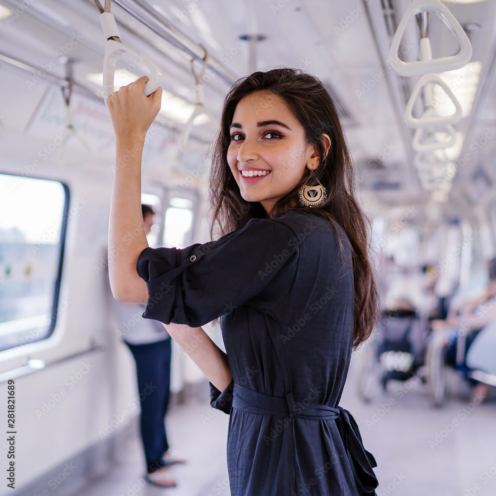 Portrait of a tall, slim, elegant, attractive, slim and beautiful Indian  Asian woman taking the train alone. She is smiling as she holds onto the  handrails. Stock Photo