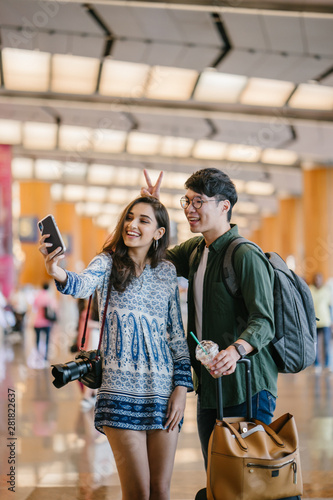 A young and diverse Asian couple  Korean man and his Indian girlfriend  take a selfie together in a new country. They have just arrived in a new country for a tour and are excited.