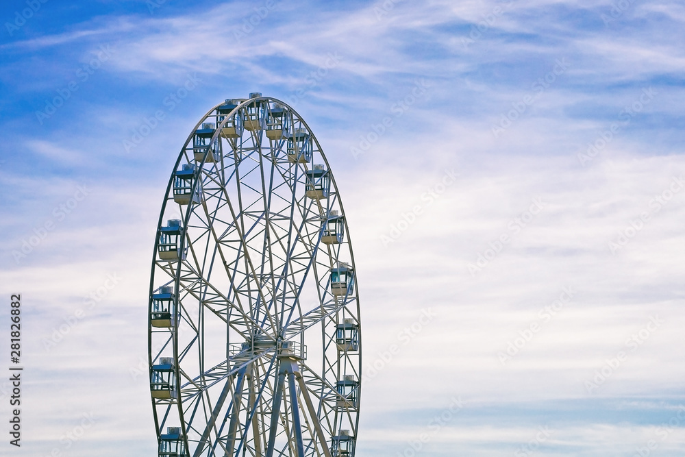 amusement ride ferris wheel on the background a blue sky with snow-white clouds amusement ride ferris wheel on the background a blue sky with snow-white clouds