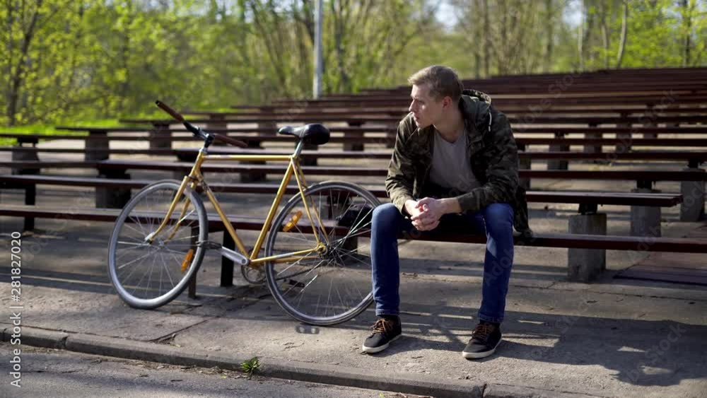 A young man sitting on a bench in a bleachers next to a yellow bicycle A young man sitting on a bench in a bleachers next to a yellow bicycle
