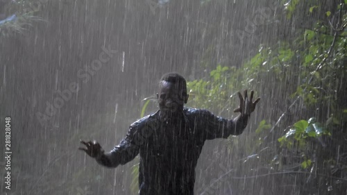 Close up slow motion shot of a happy African man dancing under the spray of a tropical waterfall while getting wet. photo