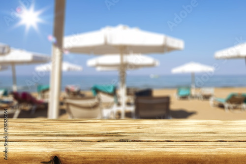 Table background with umbrellas and lounge chairs on sandy beach. Empty space for products and decoration.