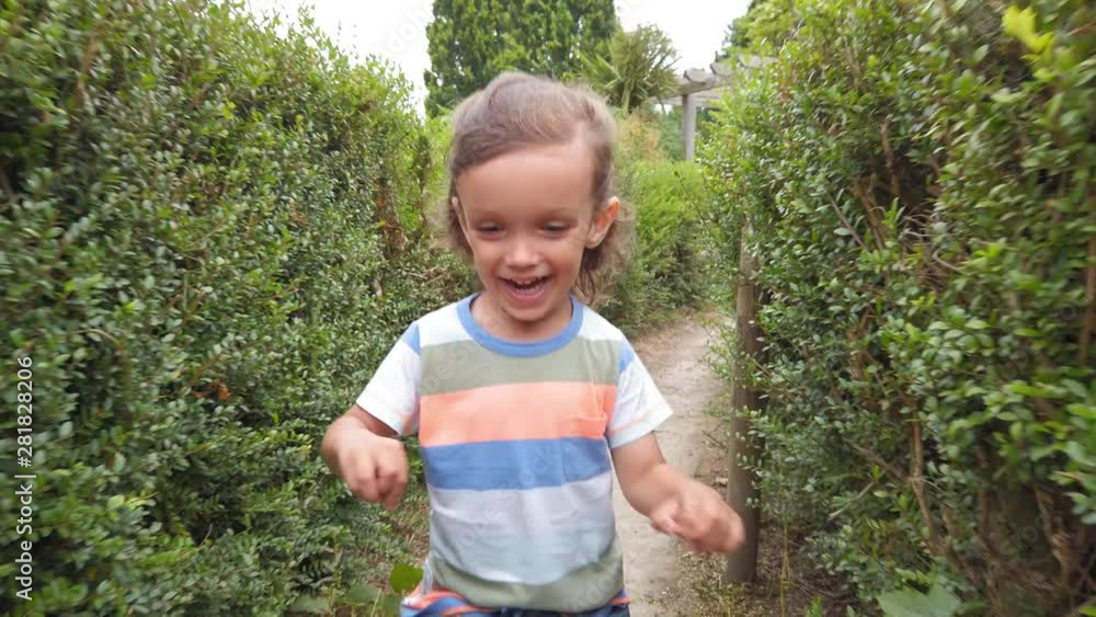 Baby boy with long hair running through a hedge maze in slow motion front view Baby boy with long hair running through a hedge maze in slow motion front view