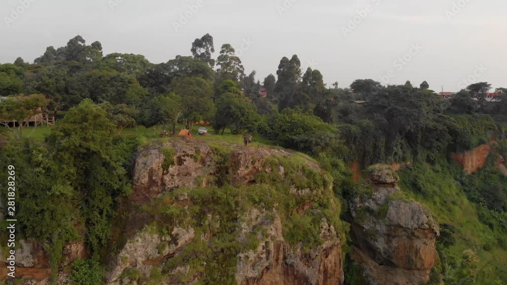 Aerial shot orbiting around two men standing on the edge of a cliff on top of a plateau in tropical East Africa. Aerial shot orbiting around two men standing on the edge of a cliff on top of a plateau in tropical East Africa.