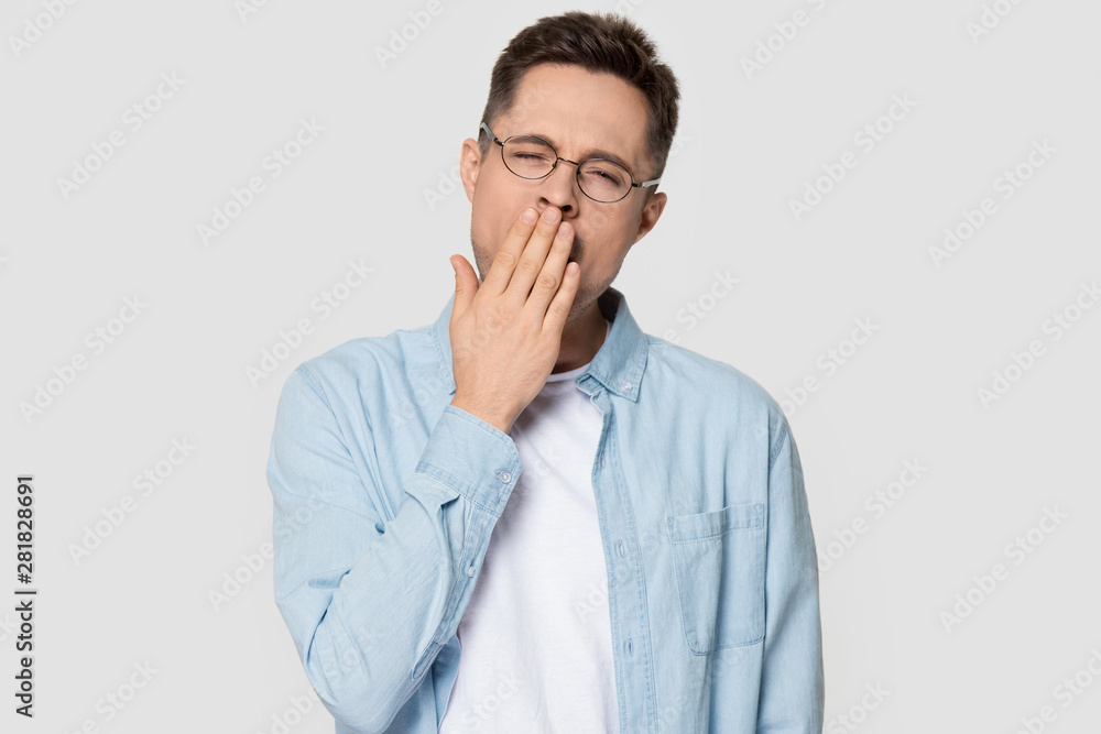 Man yawning covering mouth with hand standing on grey background Man yawning covering mouth with hand standing on grey background