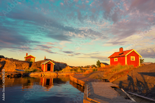 Traditional red wooden house in the island with bridge on the water at sunset clouds sky in Sweden