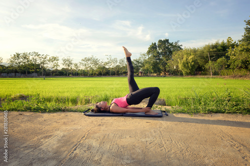 Fotografie Yoga Woman Feet Up to sky praticing pose in the rice fields farm at sunset