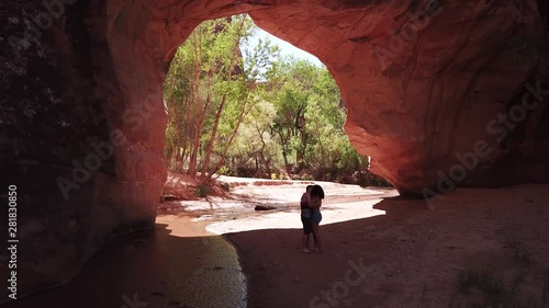 A man proposes to his girlfriend under a beautiful red rock arch in Southern Utah. She accepts and the couple share an emotional kiss and embrace. photo