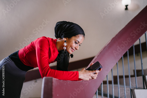 Fashion portrait of a tall, elegant and beautiful Middle Eastern Muslim woman wearing a hijab headscarf and leaning on a railing of a spiral staircase during the day. She is stylish and fashionable.