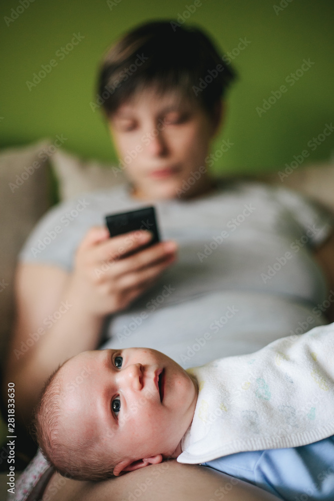 Disinterested mother playing with smartphone while guarding a small baby Disinterested mother playing with smartphone while guarding a small baby