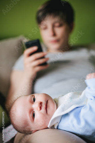 Fotografie Disinterested mother playing with smartphone while guarding a small baby