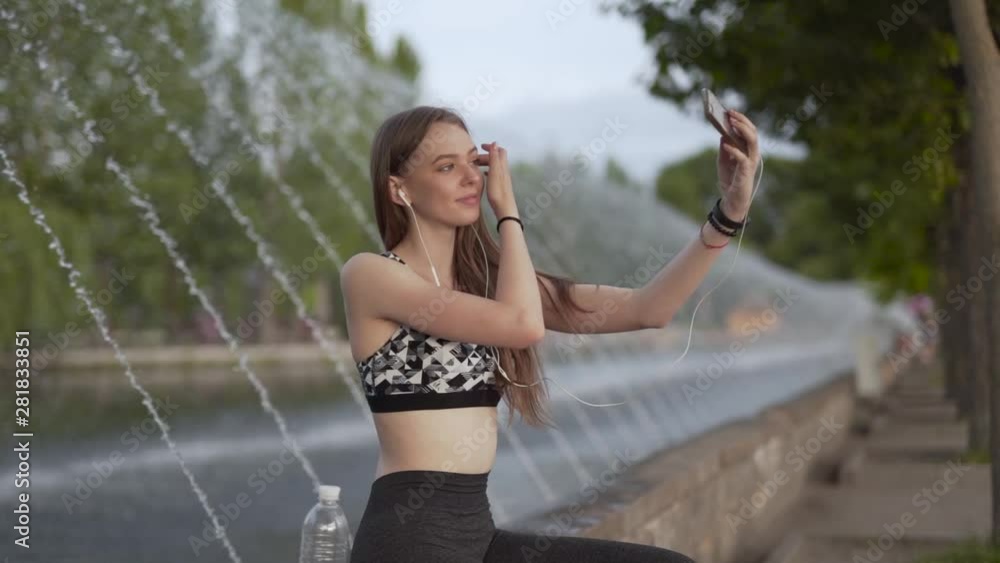 Woman in sportswear posing for a selfie next to a fountain, medium shot Woman in sportswear posing for a selfie next to a fountain, medium shot