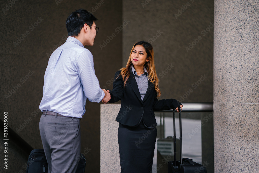 A young, tanned, beautiful and confident Asian business woman in a business suit smiles and shakes hand in agreement to mark a deal with an Asian man. They are standing in an Asia city during the day. A young, tanned, beautiful and confident Asian business woman in a business suit smiles and shakes hand in agreement to mark a deal with an Asian man. They are standing in an Asia city during the day.