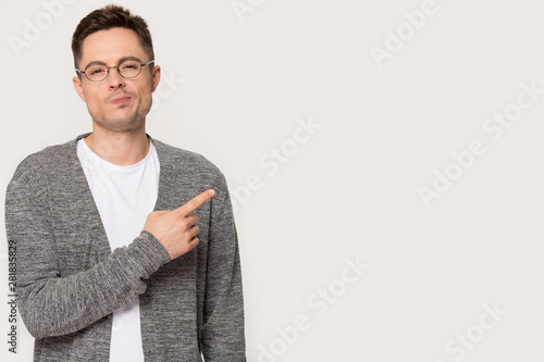 Billede på lærred Sceptic guy pose on grey background pointing finger aside copyspace