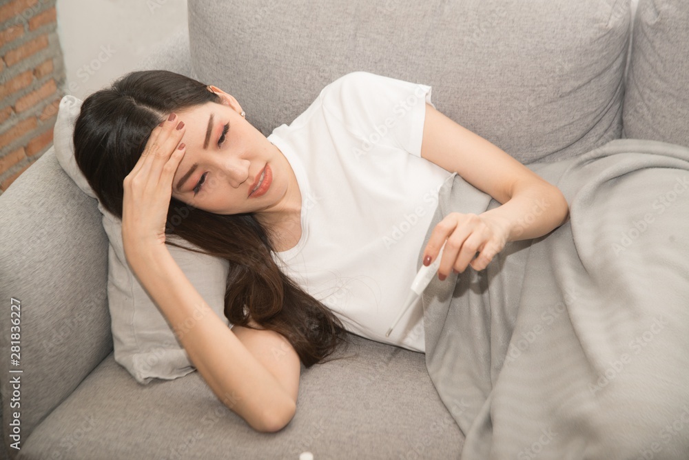 Pretty Asian woman sick from cold and used with thermometer lying on sofa in the room. Pretty Asian woman sick from cold and used with thermometer lying on sofa in the room.