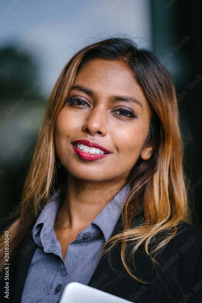 A close-up portrait of a young, tanned, beautiful and confident Southeast Asian woman in a business suit. She has a radiant smile and dyed hair and is looking intently at the camera. A close-up portrait of a young, tanned, beautiful and confident Southeast Asian woman in a business suit. She has a radiant smile and dyed hair and is looking intently at the camera.