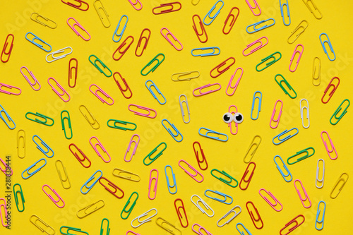 Colorful paperclips on yellow background and only one under magnifying glass
