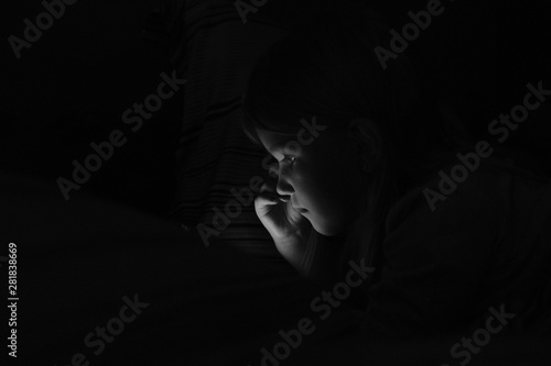 Young girl is watching something on a smart phone in a dark room with no lights