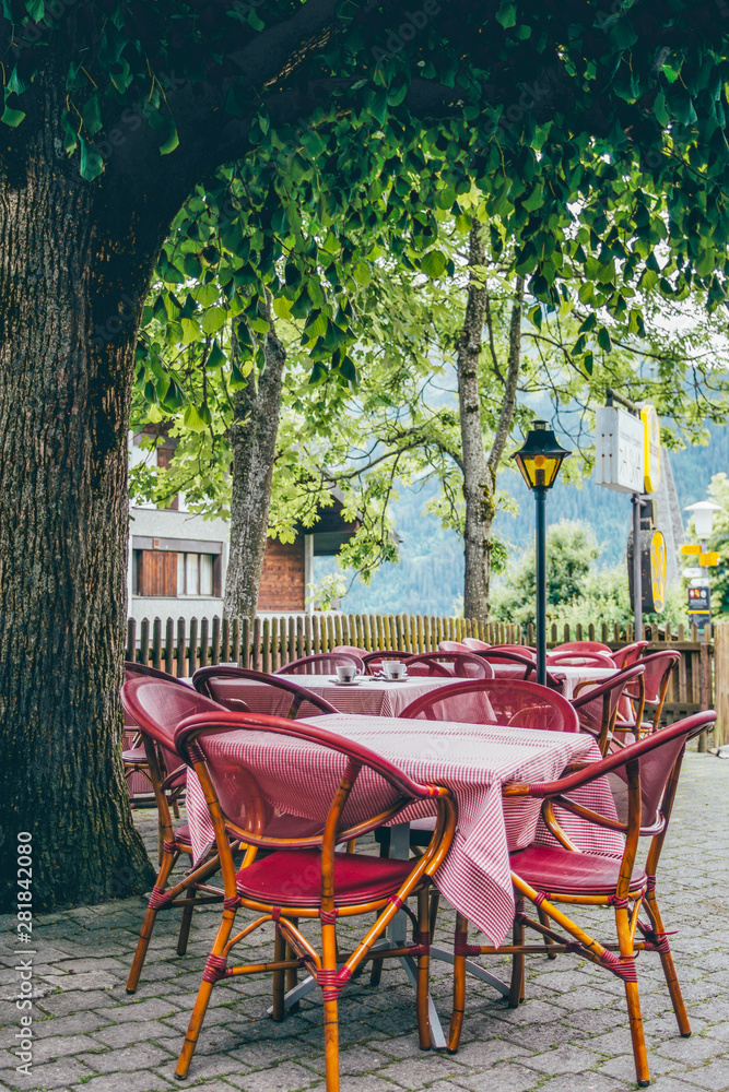 Outdoor restaurant tables with pink table cloths under a green summer tree