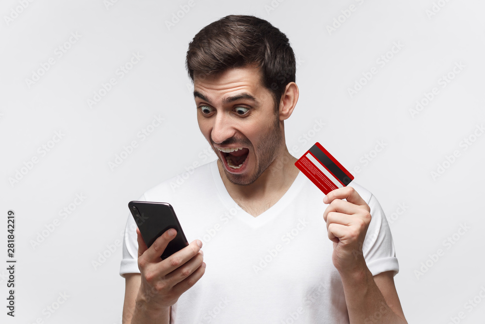Studio portrait of angry man, holding credit card and phone, shouting if he has a problem, no money or blocked bank account
