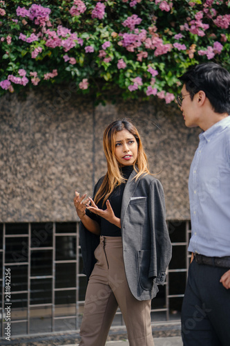 Two diverse Asian businesspeople (colleagues meeting for lunch) walking in the city and is having an animated conversation with hand gestures. One is a Korean man, the other is a Malay woman.