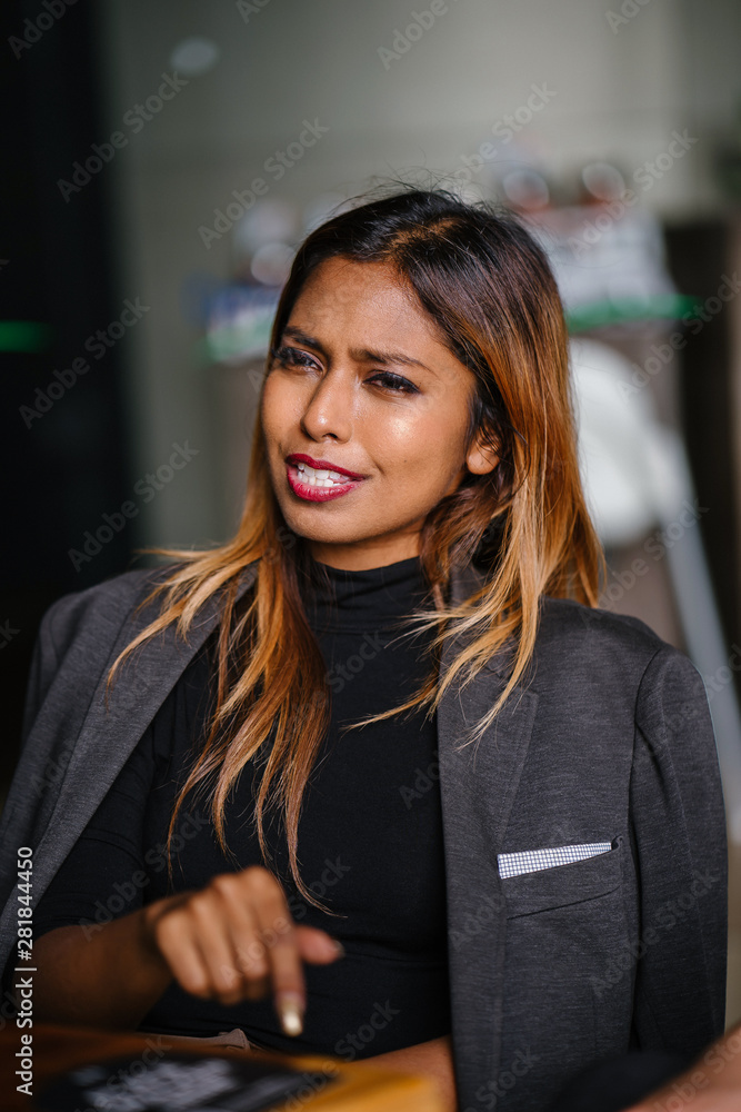 Portrait of a beautiful, fashionable, millennial Asian Malay businesswoman smiling to her colleague whose out of view and is sitting in a cafeteria during the day.