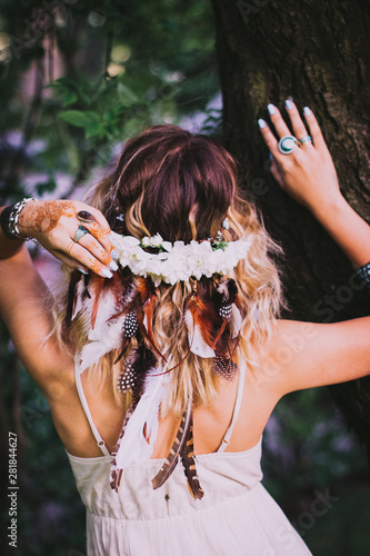 Boho style accessories. Woman with headdress made of feathers and flowers. Bohemian hippie girl in white dress.