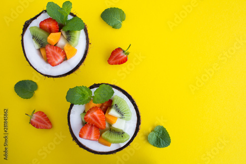 Fruit salad in the half coconut on the yellow background. Top view.Copy space.