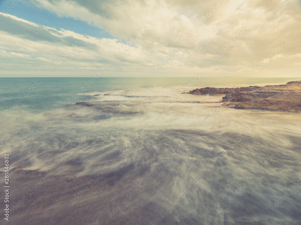 seascape at sunset with beach of rocks beaten by the sea and clouds moving in the sky