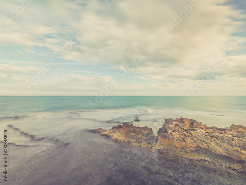 seascape at sunset with beach of rocks beaten by the sea and clouds moving in the sky