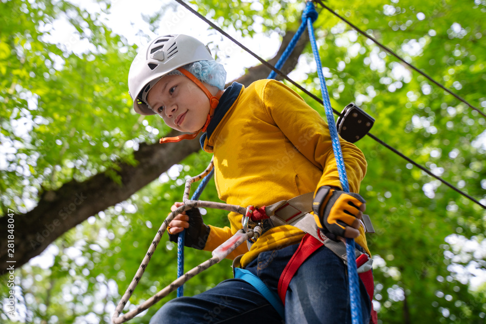 young boy in helmet in the rope park pass obstacles route high among trees, extreme sport in adventure park young boy in helmet in the rope park pass obstacles route high among trees, extreme sport in adventure park