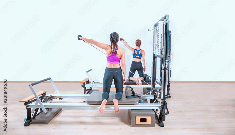 Fototapeta premium Young women exercising on pilates reformers beds