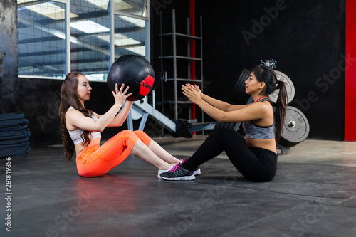 Hispanic friends doing sit-ups with a ball in the gym- Latin friends training crossfit