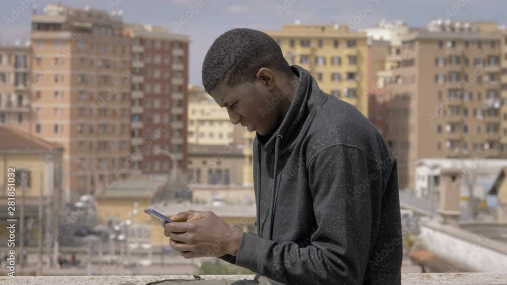 youg american african man typing on smartphone on building roof.Youth,technology youg american african man typing on smartphone on building roof.Youth,technology
