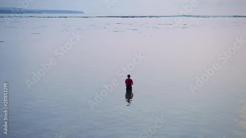 Silhouette of traditional asian fisherman is fishing in sea during low tide with small waves and blue sunset