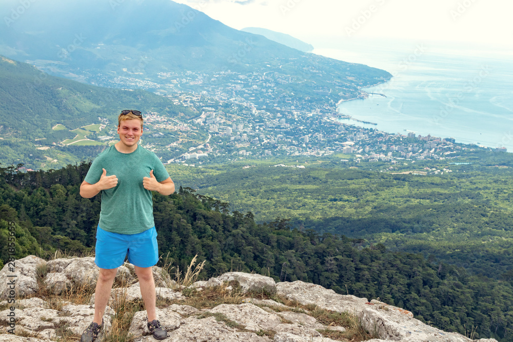 Young man standing on top of cliff in mountains and enjoying view of nature. Mountains and sea
