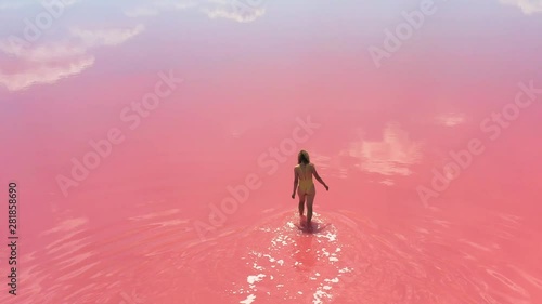 young woman going into the lake with bright pink water. Unique amazing landscape.