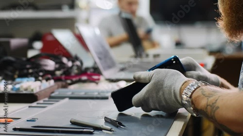 Technician finishing mobile phone repair in workshop. Repairman collects smartphone after repair by inserting all the details on workplace, hands closeup. Repair and maintenance service center. photo