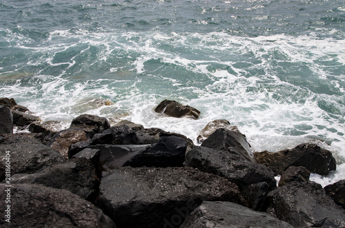 Surf waves run into black stone blocks on the shore